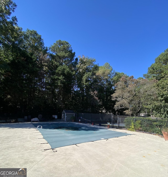 pool with a patio area, fence, and a storage unit