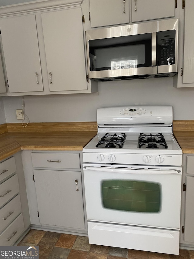 kitchen featuring stone finish floor, stainless steel microwave, white gas range, light countertops, and white cabinetry