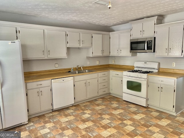 kitchen featuring white appliances, a textured ceiling, light countertops, and a sink