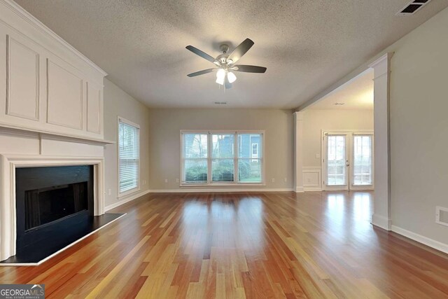 unfurnished living room with light wood-type flooring, a fireplace, visible vents, and a textured ceiling