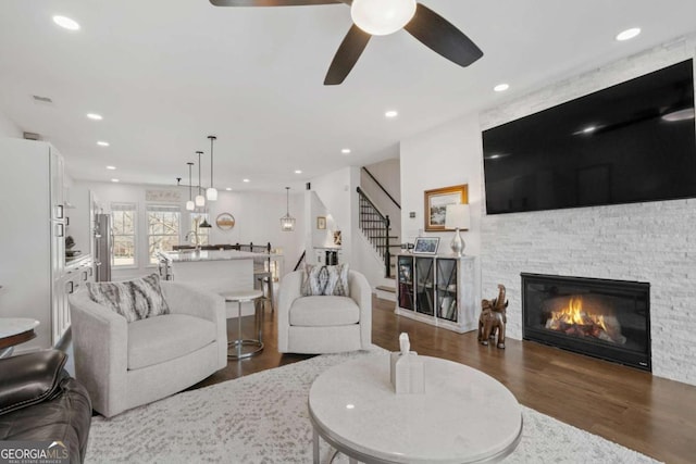 living room featuring ceiling fan, a stone fireplace, recessed lighting, dark wood-style flooring, and stairs