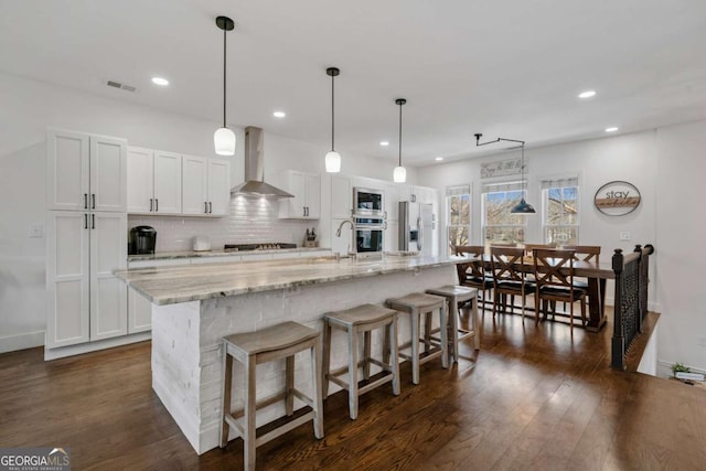 kitchen featuring dark wood-style floors, stainless steel appliances, visible vents, backsplash, and wall chimney exhaust hood