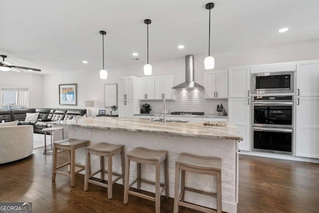 kitchen featuring white cabinetry, wall chimney range hood, appliances with stainless steel finishes, backsplash, and dark wood finished floors