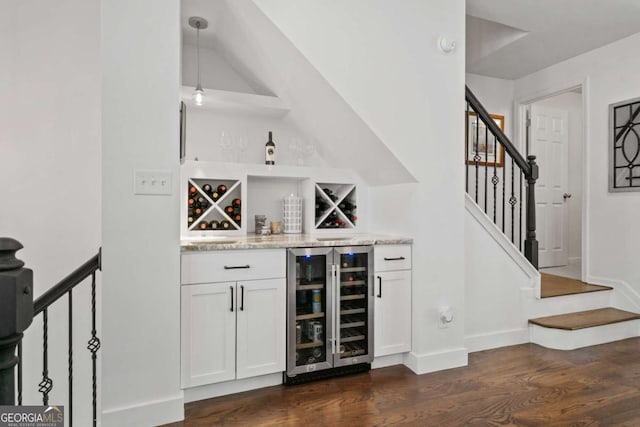 bar featuring dark wood-type flooring, beverage cooler, stairway, and a bar