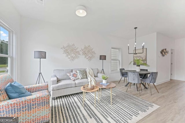 living room with a chandelier, light wood-type flooring, and baseboards