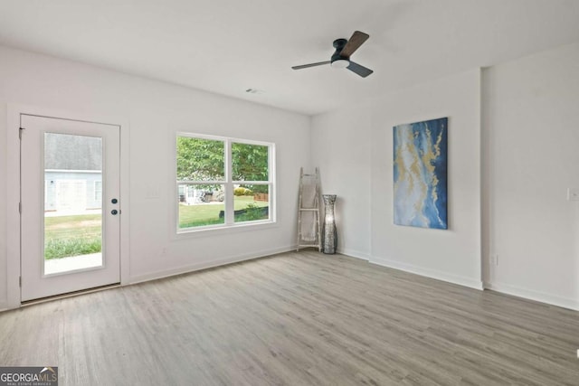 unfurnished living room with ceiling fan, plenty of natural light, wood finished floors, and baseboards