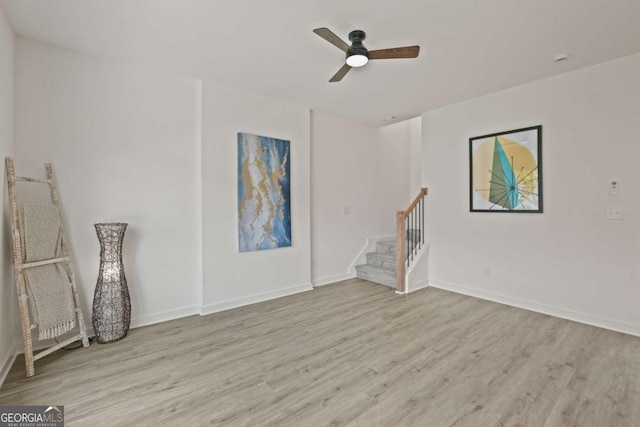 empty room featuring baseboards, ceiling fan, stairway, and wood finished floors