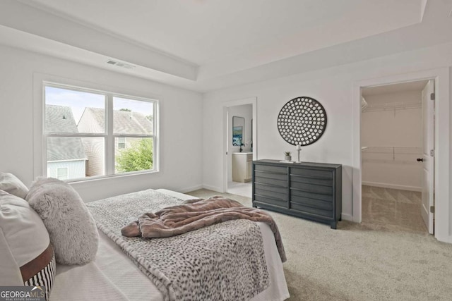 carpeted bedroom with a tray ceiling, a walk in closet, visible vents, and baseboards