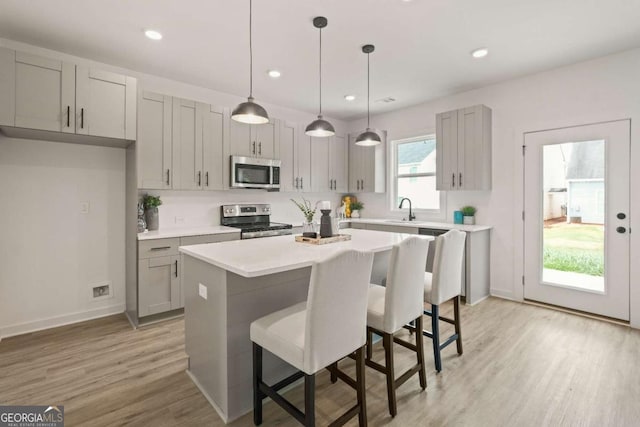 kitchen with stainless steel appliances, gray cabinets, light countertops, light wood-style flooring, and a kitchen bar