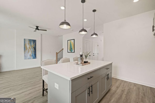 kitchen featuring light wood finished floors, a breakfast bar area, a center island, gray cabinets, and light countertops