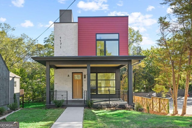 contemporary house featuring a porch, a front yard, brick siding, and a chimney