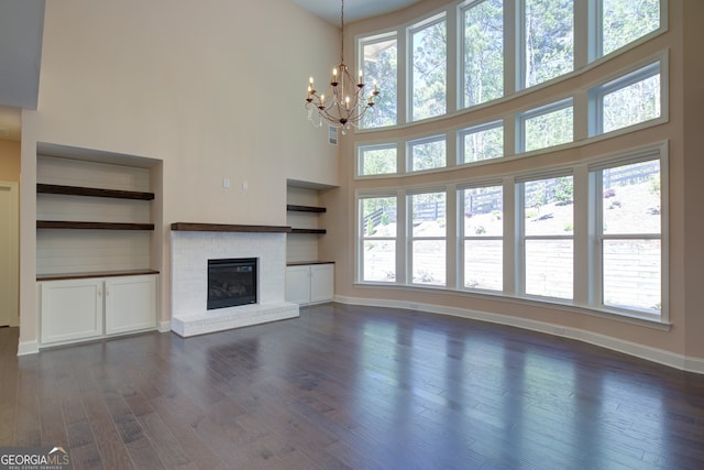 6650 Canyon Cv, Cumming, GA 30028 - unfurnished living room with a high ceiling, baseboards, dark wood finished floors, a chandelier, and a brick fireplace