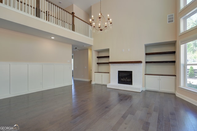 6650 Canyon Cv, Cumming, GA 30028 - unfurnished living room with a towering ceiling, a chandelier, dark wood finished floors, plenty of natural light, and a brick fireplace