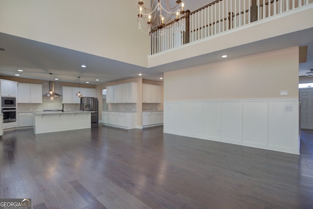 6650 Canyon Cv, Cumming, GA 30028 - unfurnished living room featuring a towering ceiling, a chandelier, dark wood-style flooring, wainscoting, and a decorative wall