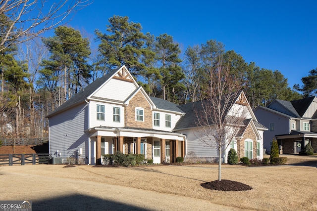 traditional-style house with stone siding, fence, covered porch, and cooling unit