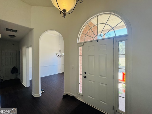 entryway featuring arched walkways, a notable chandelier, dark wood-style flooring, visible vents, and baseboards