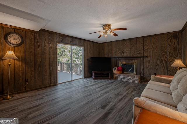 living area featuring dark wood-type flooring, a brick fireplace, ceiling fan, wooden walls, and a textured ceiling