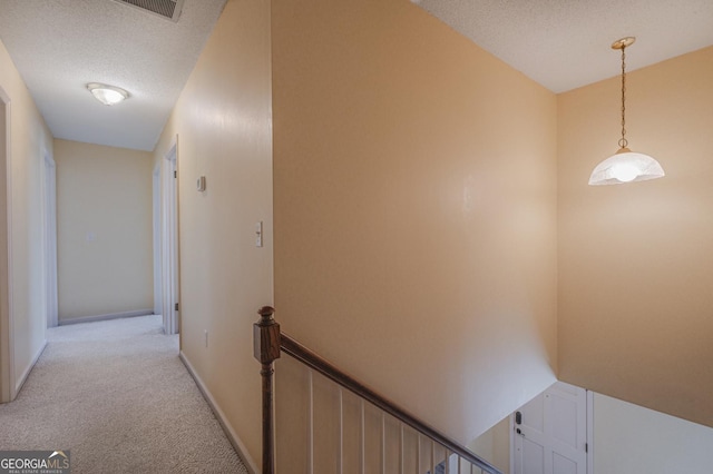 hall with baseboards, light carpet, a textured ceiling, and an upstairs landing