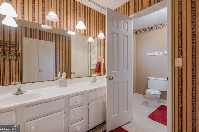 full bath featuring double vanity, a sink, toilet, and wallpapered walls