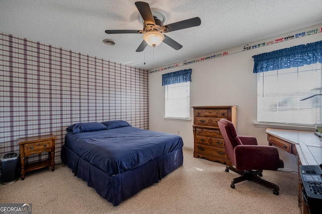 carpeted bedroom featuring wallpapered walls, a ceiling fan, visible vents, and a textured ceiling