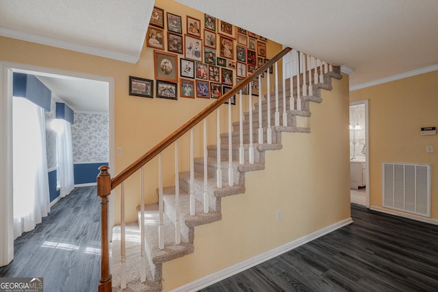 staircase with wallpapered walls, wood finished floors, visible vents, and crown molding