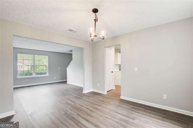 unfurnished room with visible vents, baseboards, wood finished floors, an inviting chandelier, and a textured ceiling