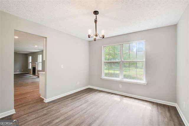 unfurnished room featuring a fireplace, a textured ceiling, baseboards, and wood finished floors