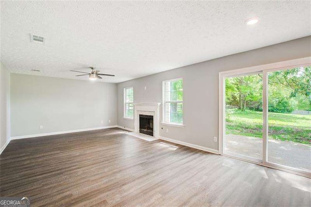 unfurnished living room with a fireplace with flush hearth, visible vents, baseboards, and wood finished floors