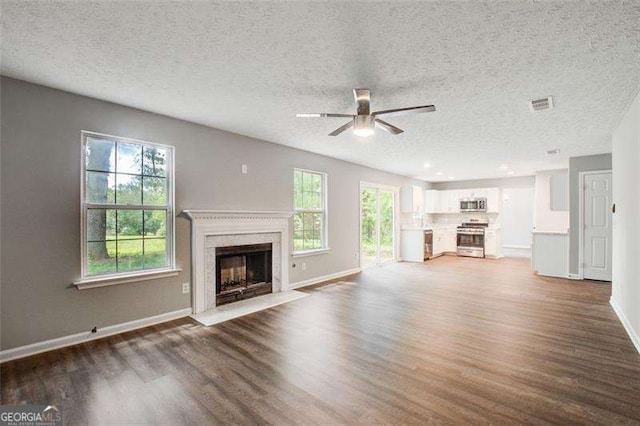 unfurnished living room featuring a ceiling fan, a fireplace with flush hearth, visible vents, and wood finished floors