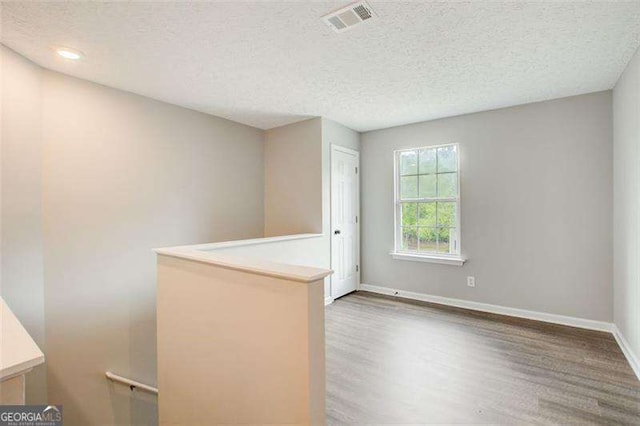 spare room with baseboards, a textured ceiling, visible vents, and wood finished floors