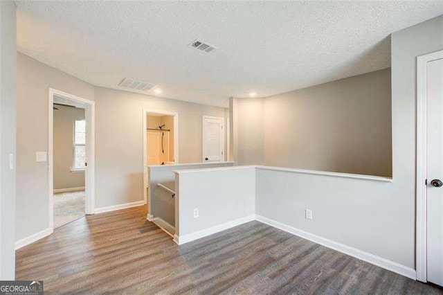 spare room featuring a textured ceiling, wood finished floors, visible vents, and baseboards