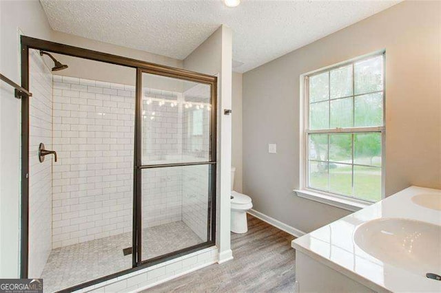 bathroom with a textured ceiling, wood finished floors, a shower stall, and toilet