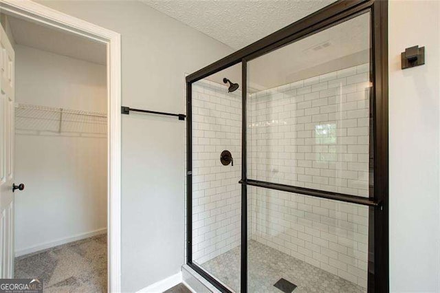 full bathroom featuring a textured ceiling, a spacious closet, a shower stall, and baseboards