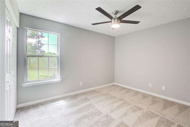 empty room with a textured ceiling, ceiling fan, carpet, and baseboards