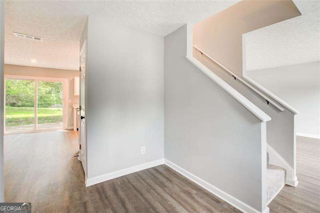 interior space featuring visible vents, a textured ceiling, baseboards, and wood finished floors