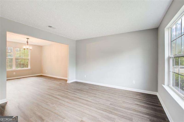 empty room featuring a chandelier, baseboards, wood finished floors, and a healthy amount of sunlight