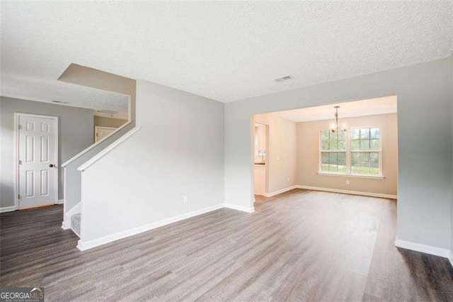 unfurnished living room with wood finished floors, a textured ceiling, baseboards, and stairs