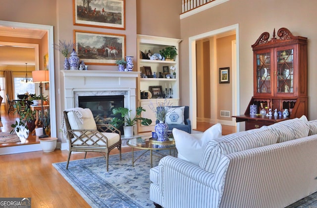 living room with built in shelves, visible vents, a premium fireplace, wood finished floors, and baseboards