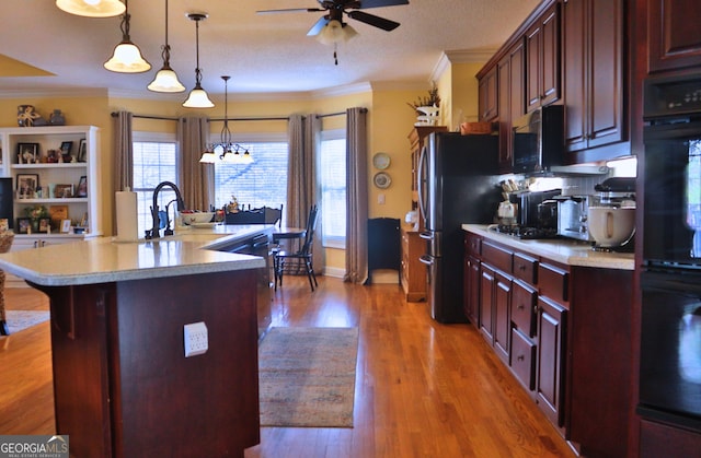 kitchen featuring crown molding, a center island with sink, light countertops, ceiling fan, and wood finished floors