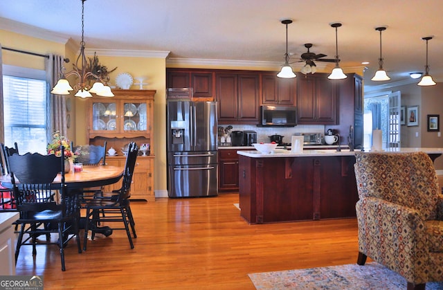 kitchen featuring stainless steel appliances, hanging light fixtures, light countertops, light wood finished floors, and crown molding