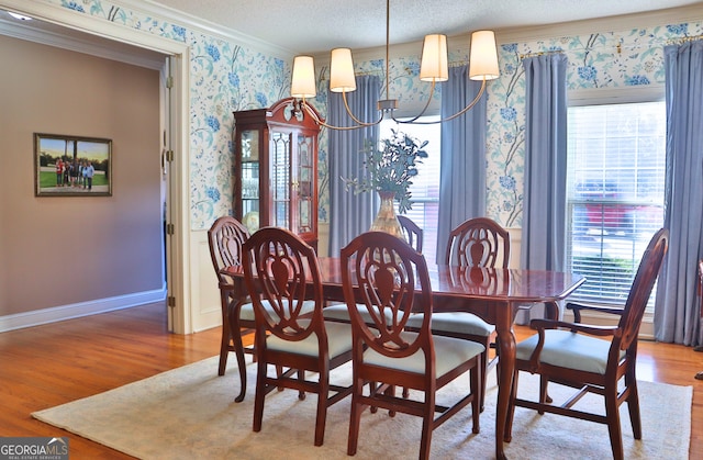 dining space with ornamental molding, wood finished floors, a textured ceiling, and wallpapered walls