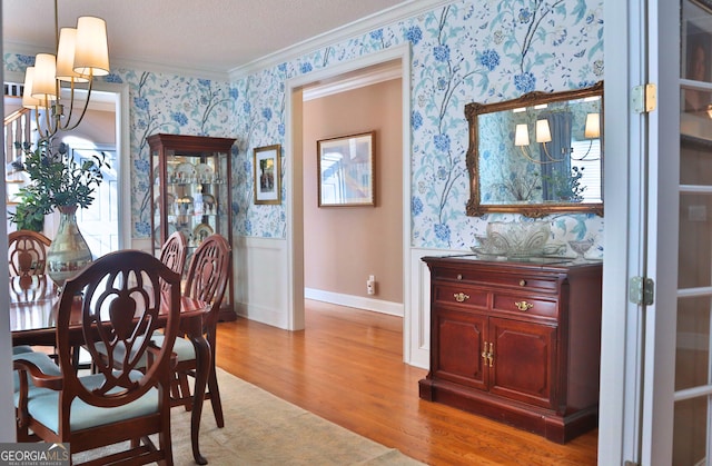 dining room with wallpapered walls, a wainscoted wall, ornamental molding, wood finished floors, and a notable chandelier