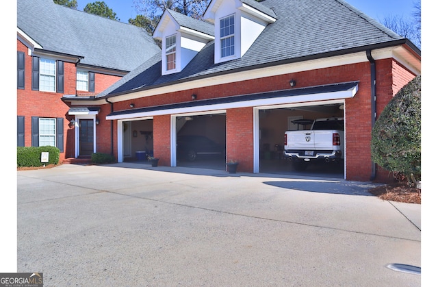 exterior space with driveway, brick siding, an attached garage, and a shingled roof