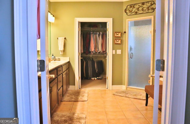 full bath with baseboards, tile patterned flooring, a spacious closet, vanity, and a shower stall