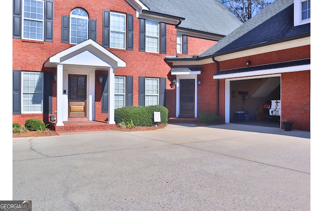 doorway to property featuring driveway, brick siding, roof with shingles, and an attached garage