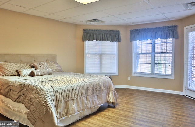 bedroom featuring a paneled ceiling, visible vents, baseboards, and wood finished floors