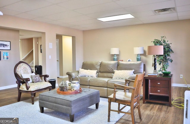 living area with a paneled ceiling, baseboards, visible vents, and wood finished floors