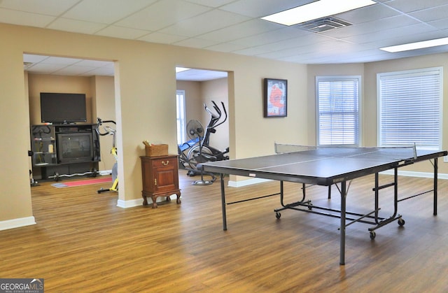 recreation room with a paneled ceiling, wood finished floors, visible vents, and baseboards