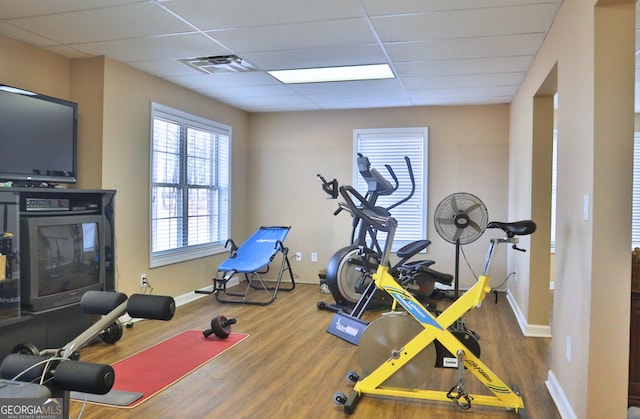 workout room featuring a paneled ceiling, visible vents, baseboards, and wood finished floors