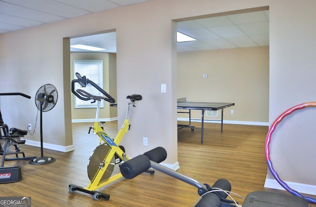 workout room featuring wood finished floors, a paneled ceiling, and baseboards